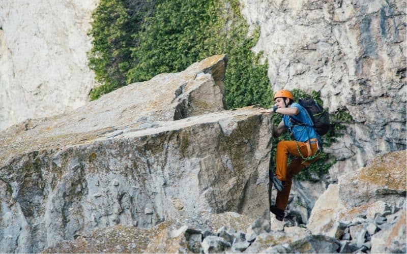 Climber climbing over a rock face wearing a backpack