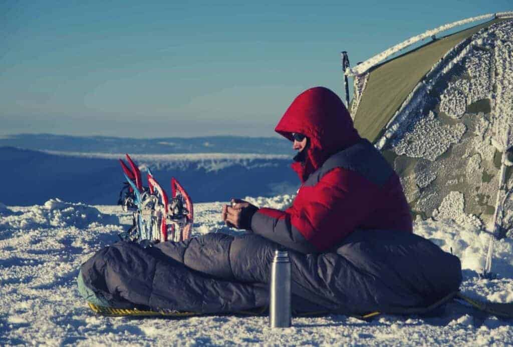 A man sitting in the snow in a sleeping bag