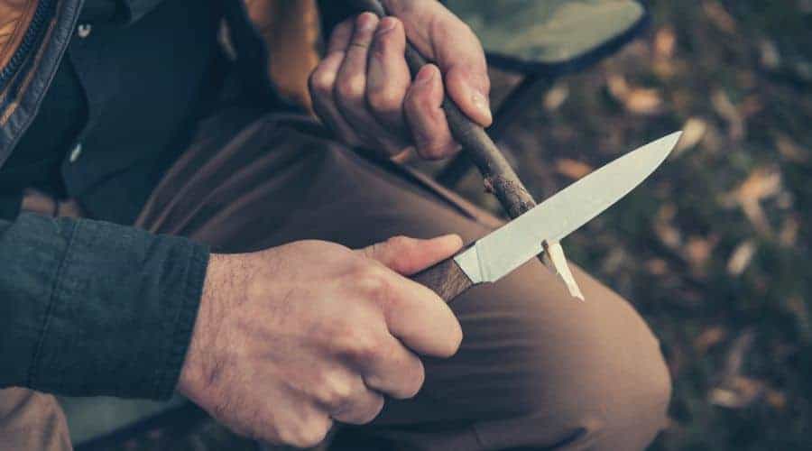 man whittling stick with knife intext