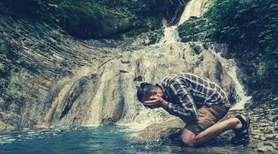 A young hiker kneels by the falls and washed his face intext