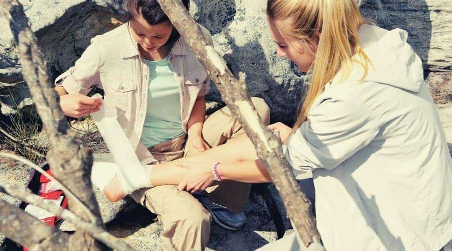 woman hiker wraps bandage around injured ankle of other hiker