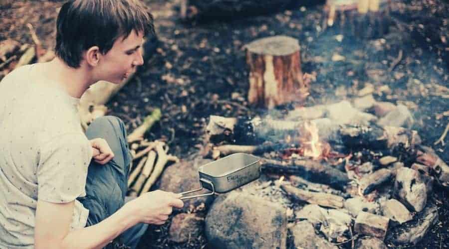 Man putting frying pan into smoky campfire.