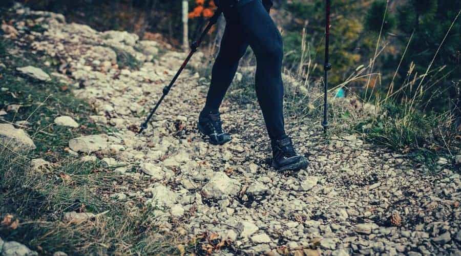 Woman hiking in trail of stones with leggings and hiking poles