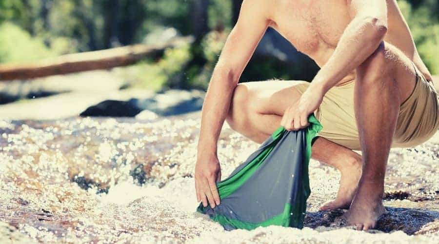 Camping hiker man on trek washing clothes in river intext