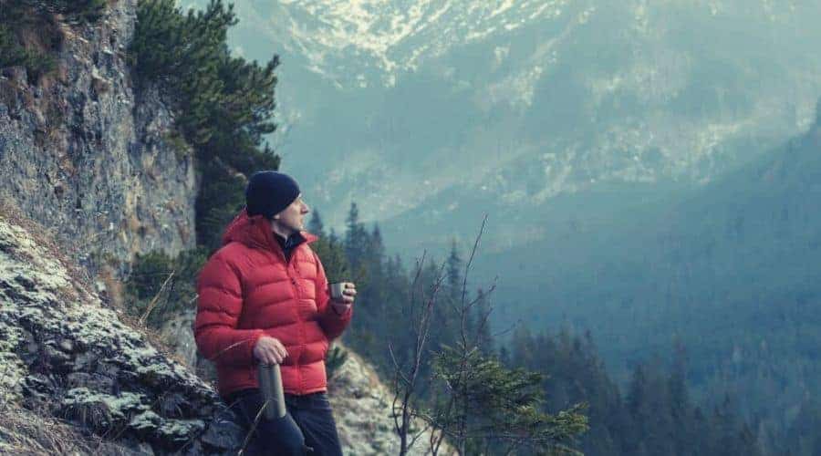 Hiker drinking from thermos flask on mountainside intext