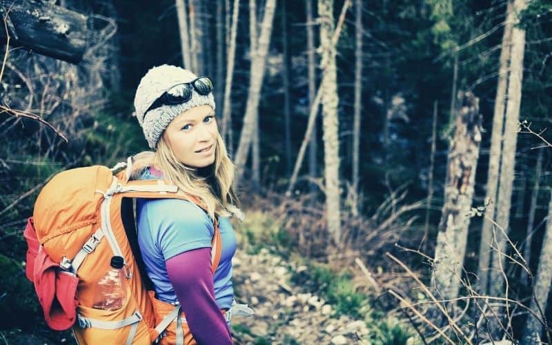 Woman hiking in winter cold dark winter forest in warm hiking clothing
