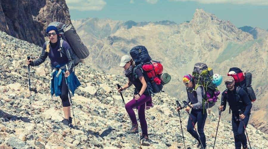 group of hikers with trekking poles walking up mountain scree slopehiking clothing intext