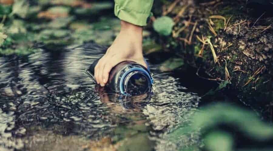 woman hiker taking water from a river intext