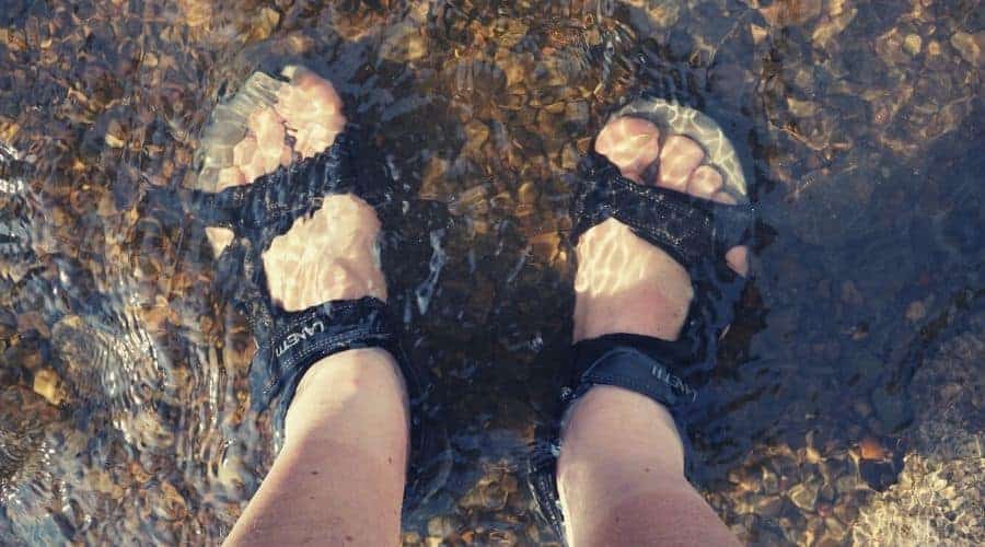 Hikers feet in sandals standing in shallow river