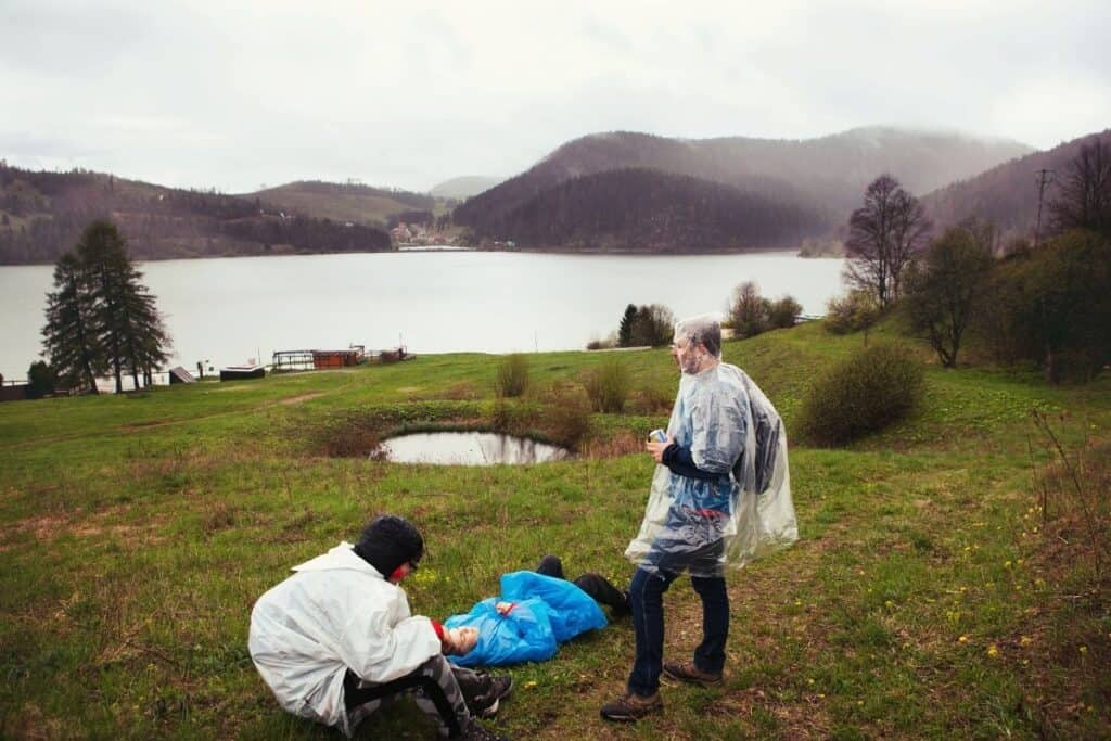 Men wearing ponchos in the rain in front of a lake and mountain scenery