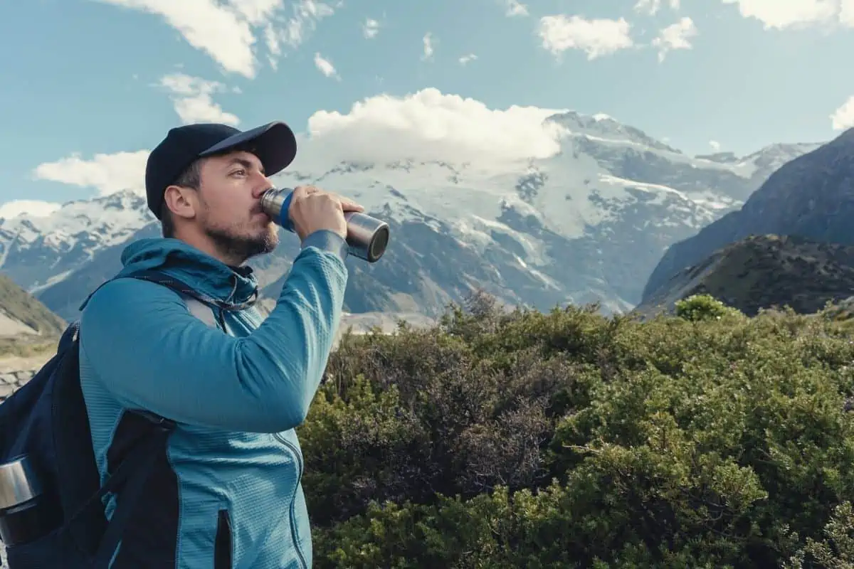 Man drinking from water flask in front of a mountain
