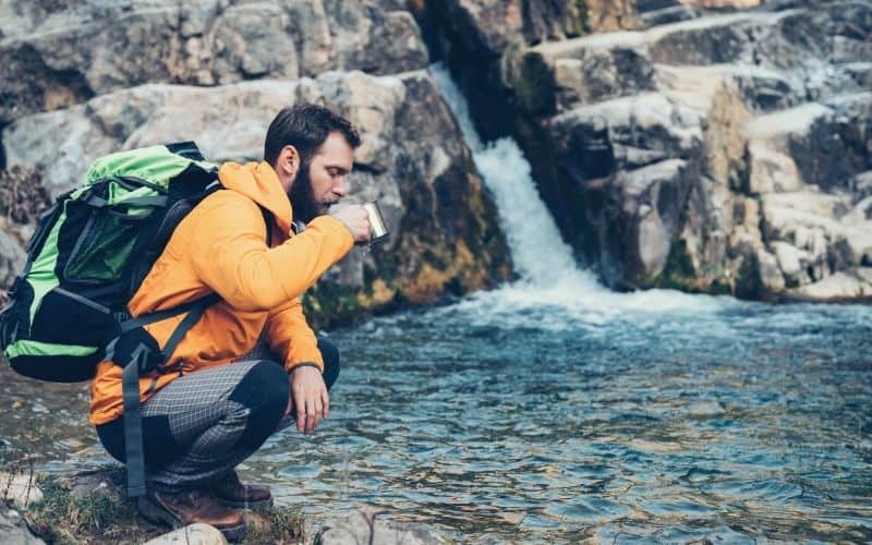 Hiker drinking water directly from a stream