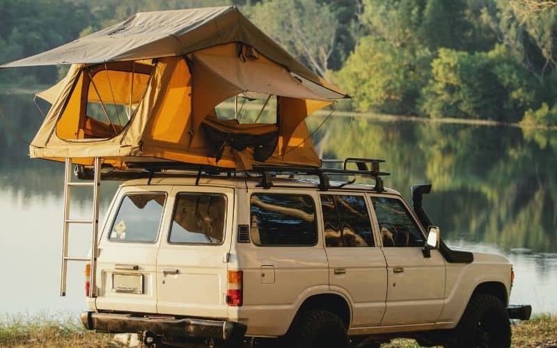 Roof top tent pitched on a truck in front of a lake