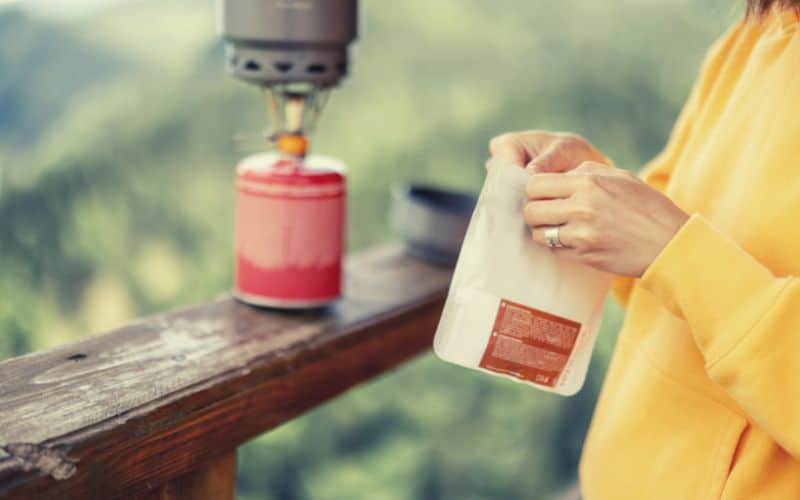 Woman opening freeze dried food packet with stove in background