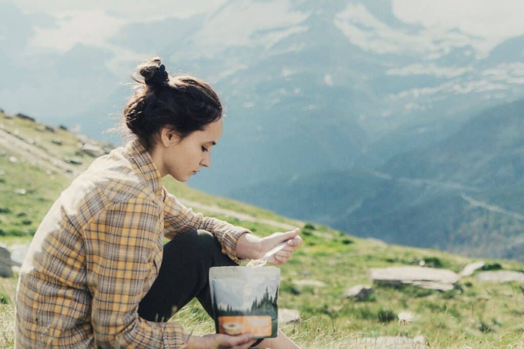 Backpacker eating freeze dried packet of food on mountainside