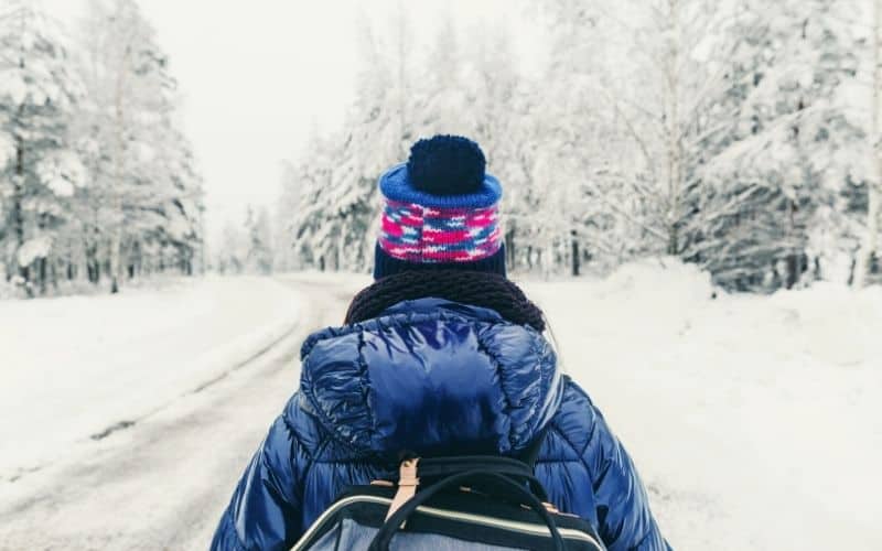 female hiker in down jacket walking in snowy forest in sweden