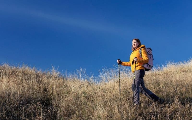 female hiker on grassy hill in down jacket with poles