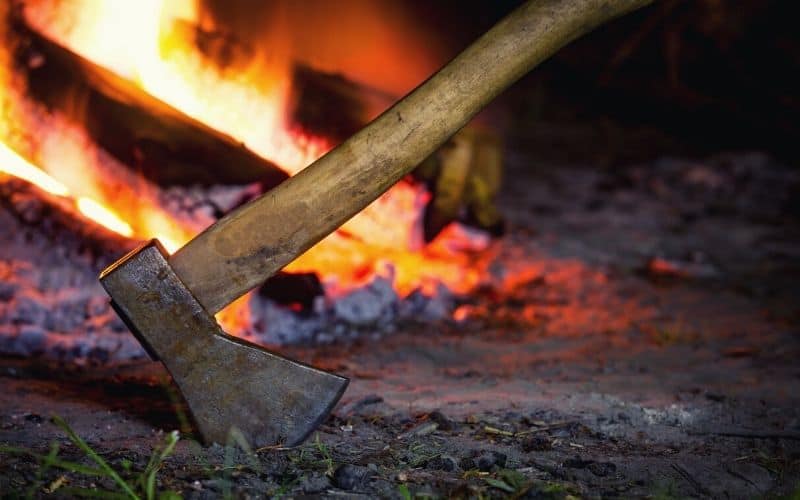 Axe struck into the ground in front of a campfire