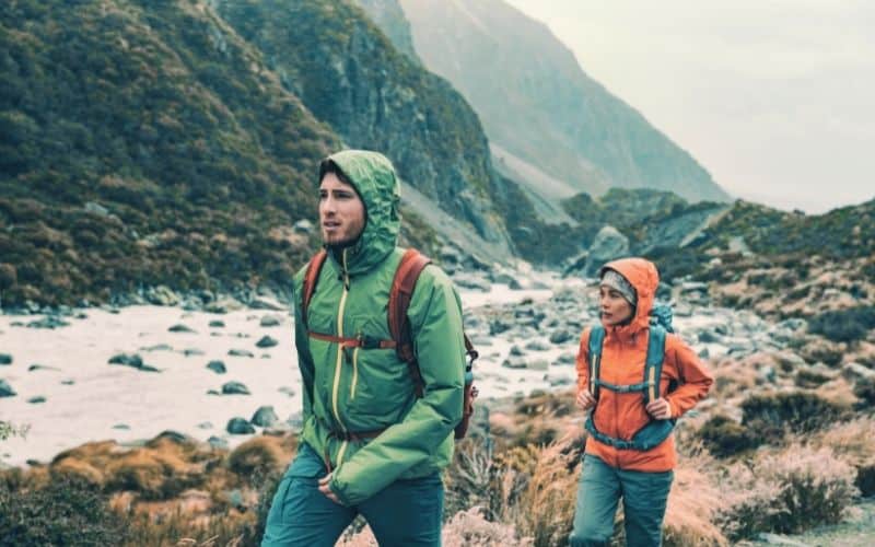 two hikers hiking in rain through valley