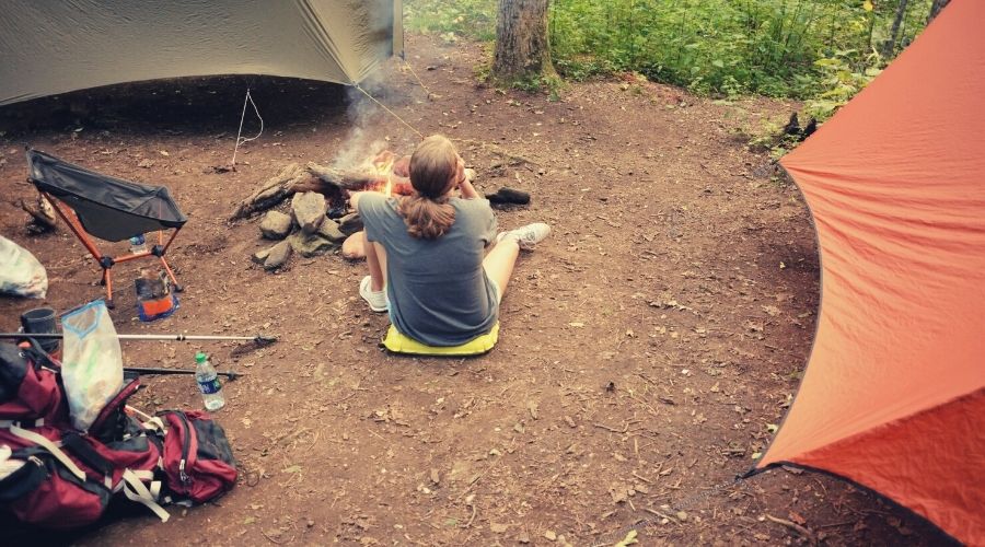 backpacker next to fire two hammocks with tarps