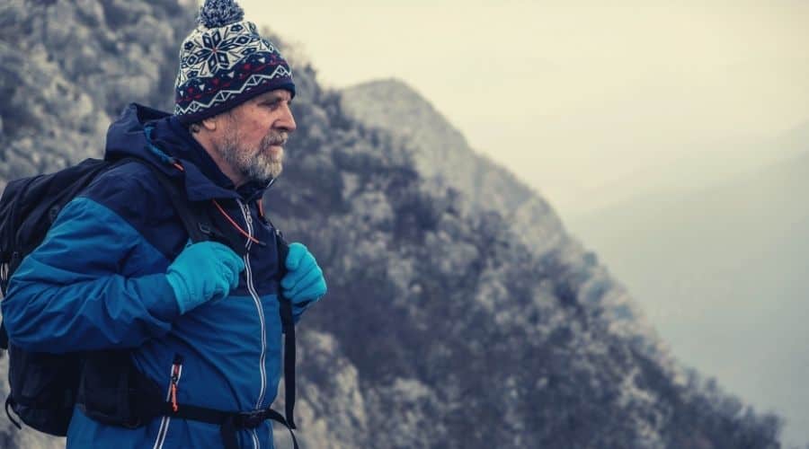 older hiker wearing gloves hat and jacket looking out from mountain