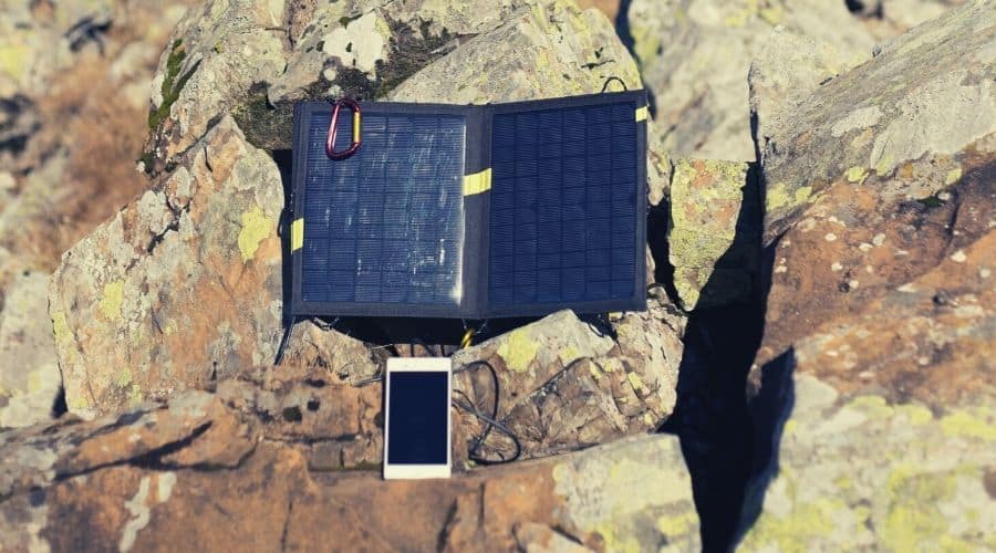 portable solar panel charging phone on rocky hillside