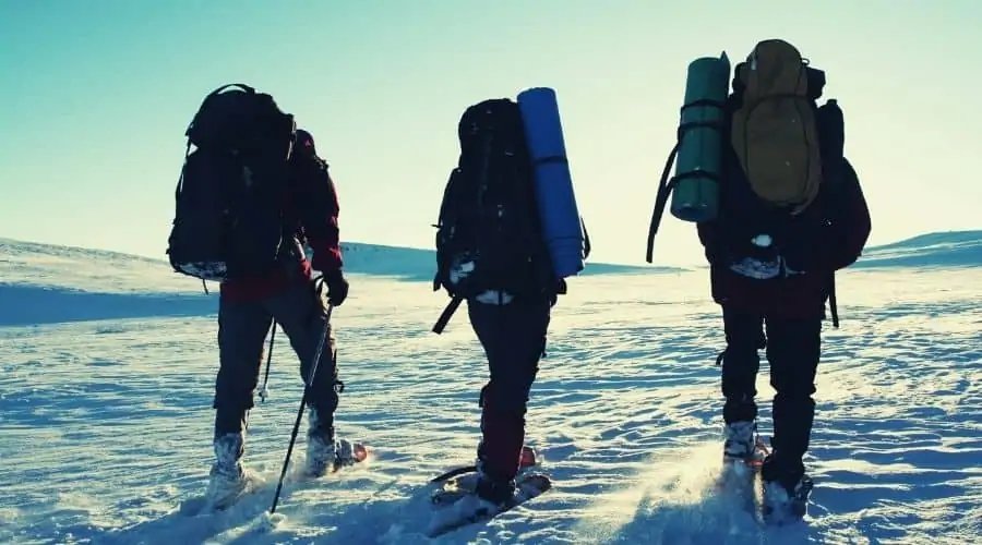 three hikers in snowshoes hiking across snow field