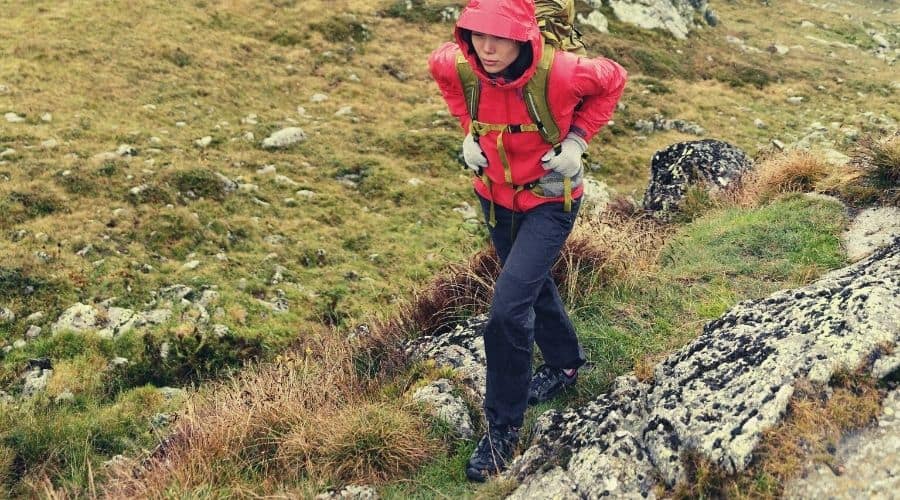woman hiker in rain gear climbing grassy hill
