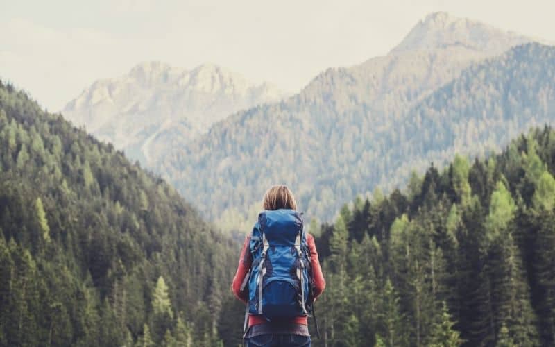 Backpacker wearing backpack looking out at forest filled mountains