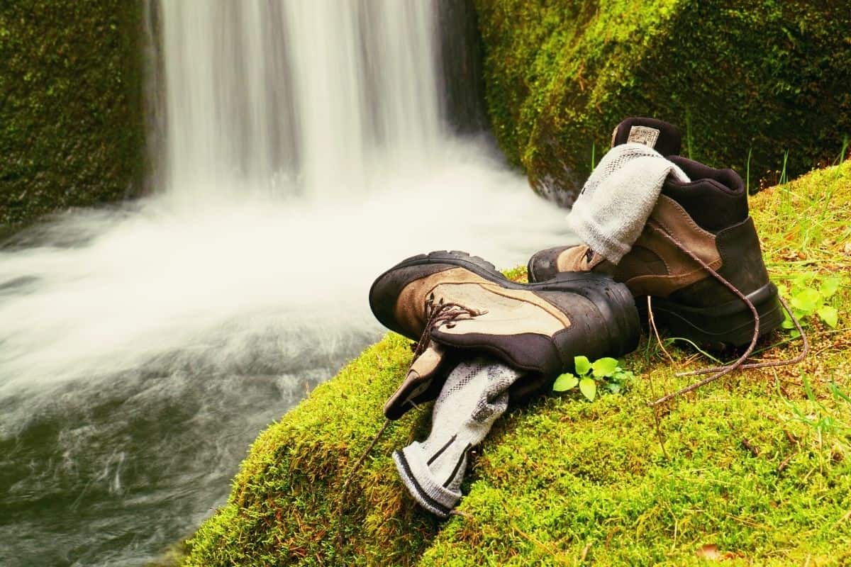 Hiking socks and boots on mossy patch in front of waterfall
