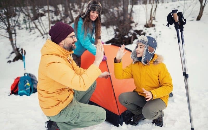 Dad high-fiving his son in front of a tent pitched in snow