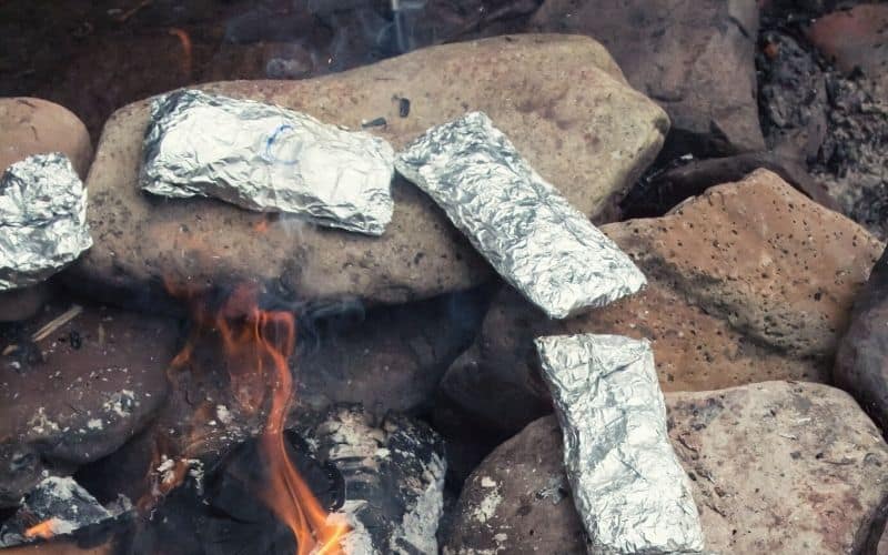Foil packets on stones around a campfire