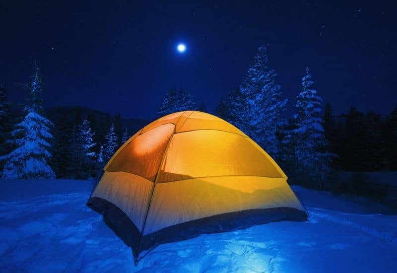 Lit up tent pitched in the snow under a full moon