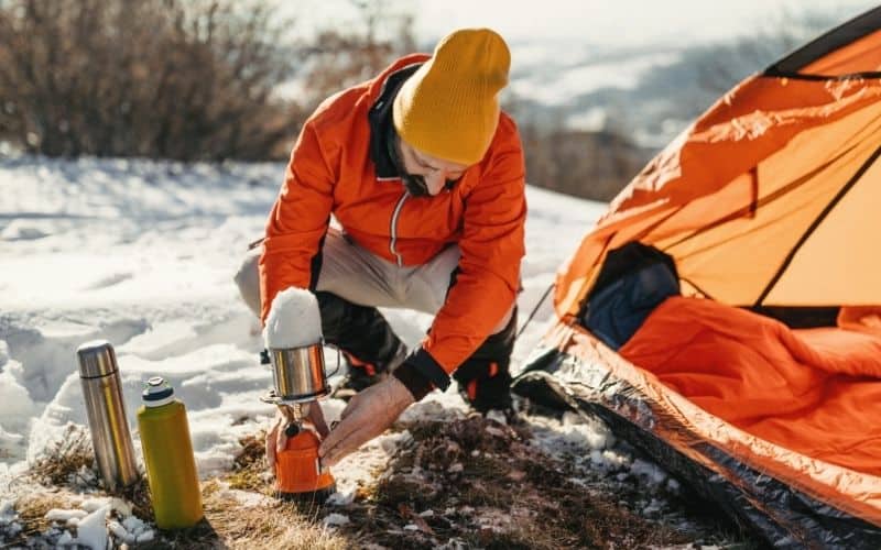 Man sitting outside tent using a camping stove to melt snow