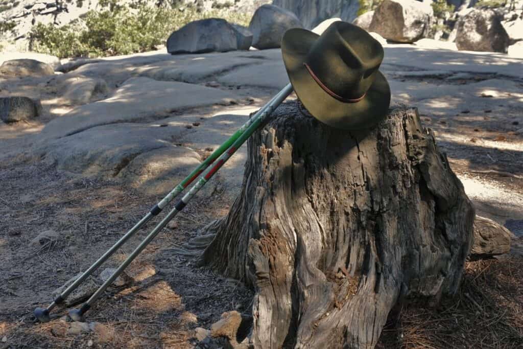 A hiking hat propped up on trekking poles against a tree stump