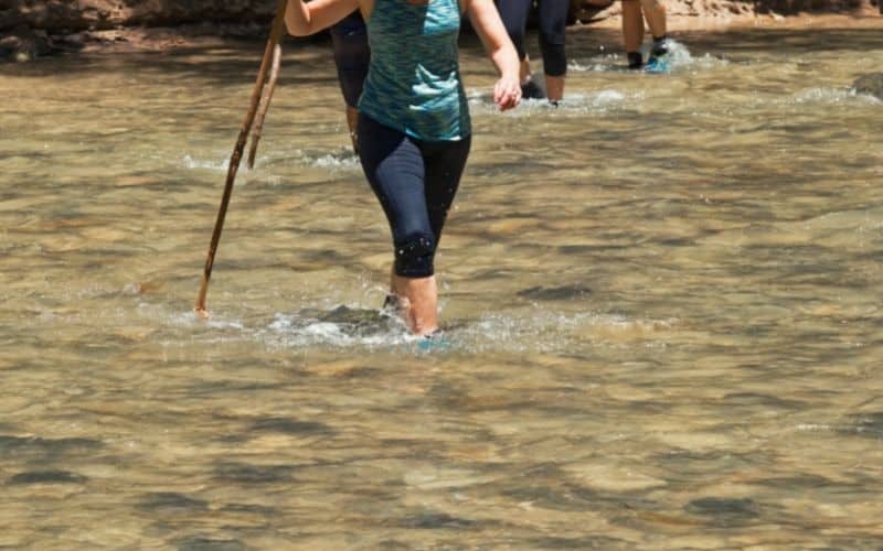 female hiker crossing stream in leggings