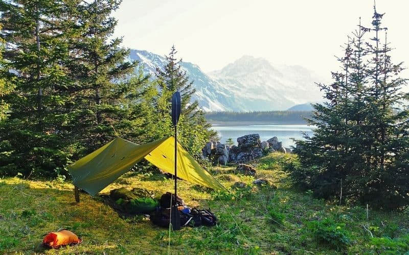 Tarp pitched at a lakeside in front of snowy mountains