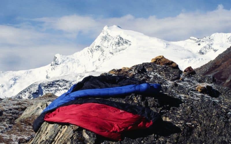 two sleeping bags on rock surface with snowy mountains in background