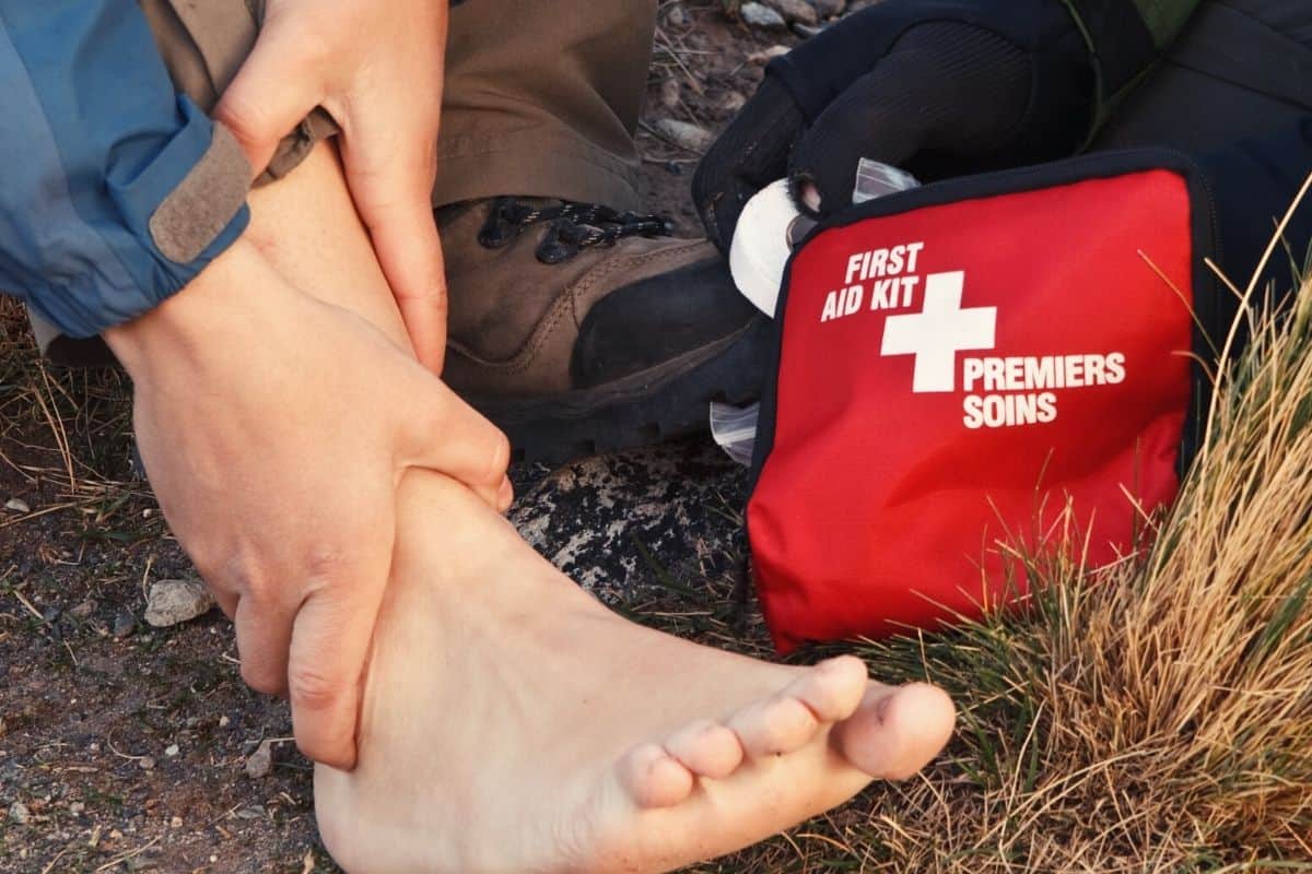 Man with boot off holding his swollen ankle beside a first aid kit