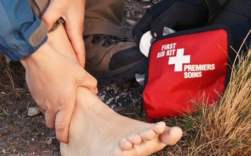 Man with boot off holding his swollen ankle beside a first aid kit
