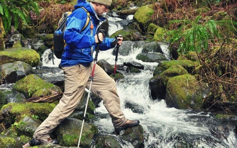 hiker crossing stream in hiking boots with trekking poles