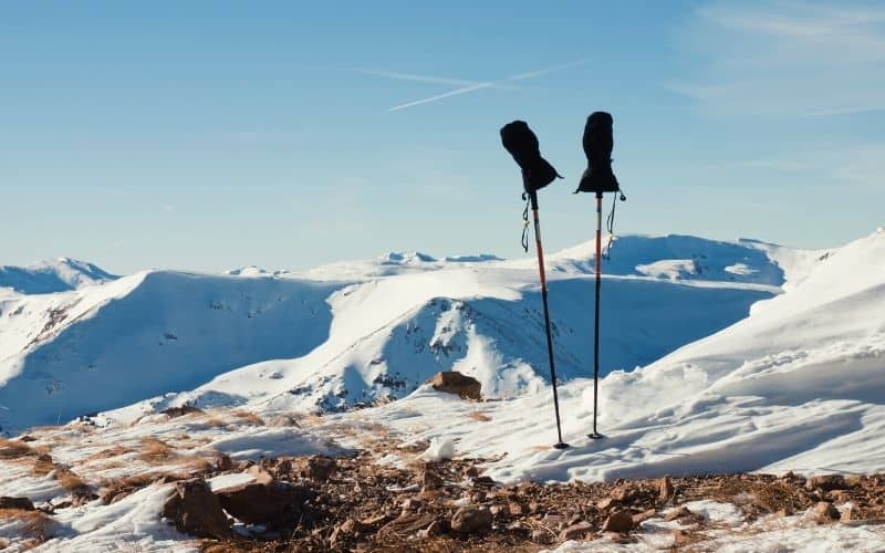 A pair of mittens are sat on top a pair of hiking poles on a snowy mountaintop