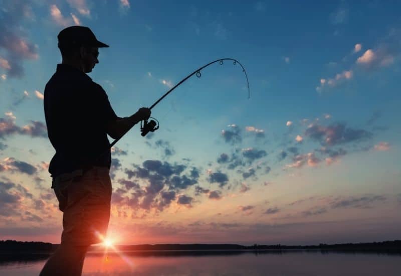 Silhouette of a man fishing against a sunrise