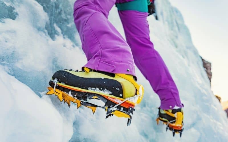 Close up of person climbing an icy face wearing snow shoes with crampons attached