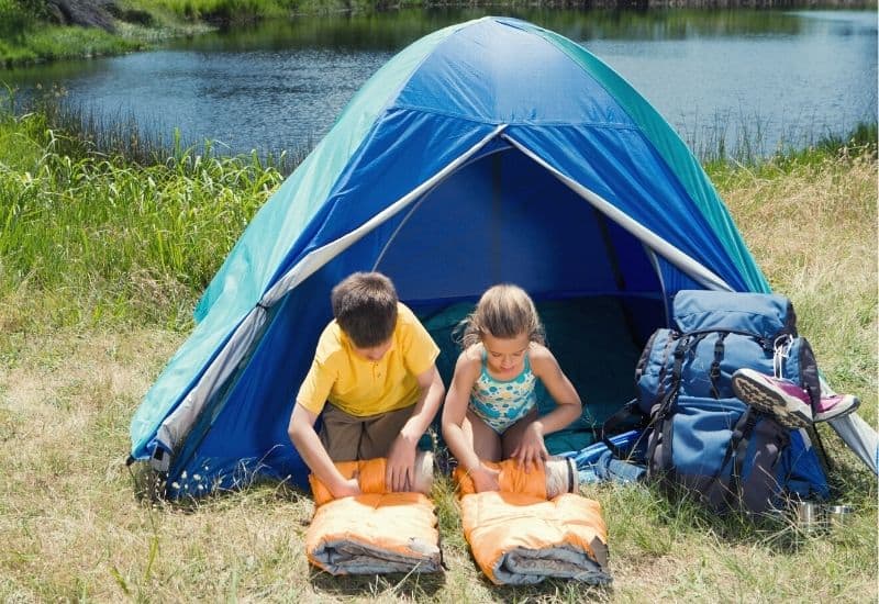 Children roll up sleeping bags in front of their tent