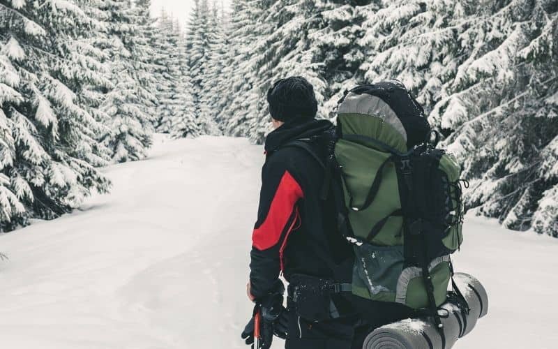 Man walking through the snow carrying camping gear on his back