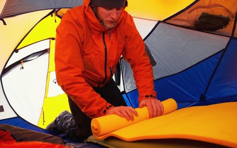 Man rolling up sleeping pad inside tent