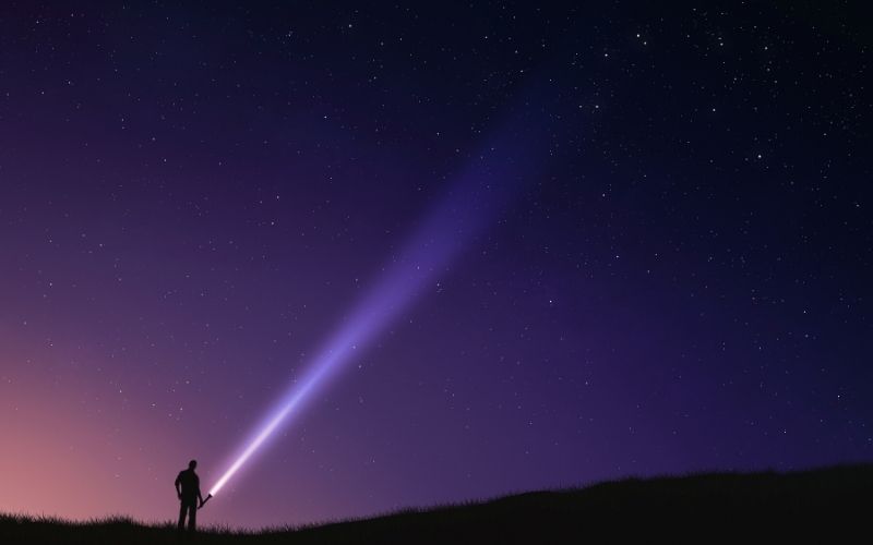 Man shining torch into the starry night sky