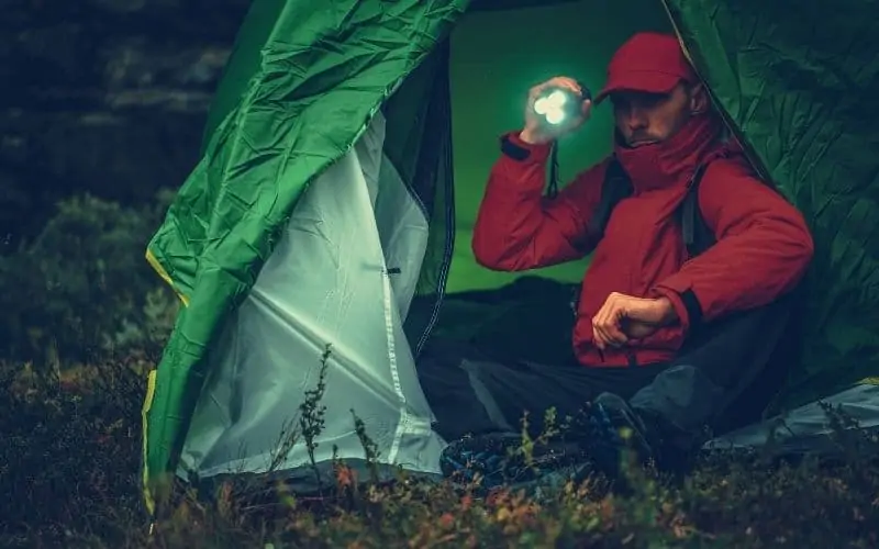 Man sitting in tent shining a flashlight outside
