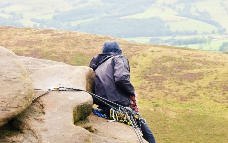 Man sitting on cliff edge in rain jacket holding climbing ropes